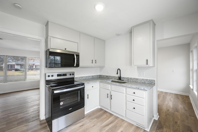 kitchen featuring a sink, white cabinetry, baseboards, appliances with stainless steel finishes, and light wood-type flooring