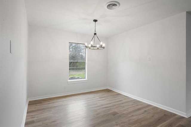 unfurnished room with an inviting chandelier, wood finished floors, visible vents, and baseboards