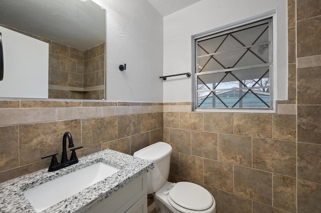 bathroom featuring toilet, a wainscoted wall, tile walls, and vanity