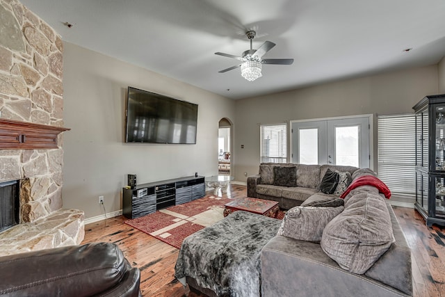 living room featuring baseboards, a fireplace, french doors, hardwood / wood-style flooring, and arched walkways