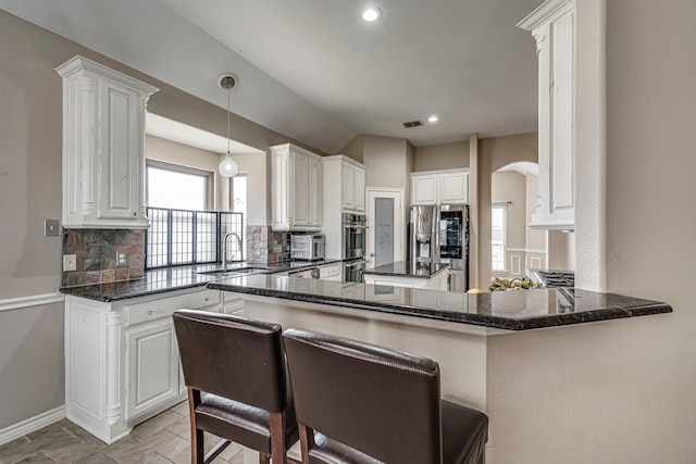 kitchen with dark stone countertops, arched walkways, tasteful backsplash, and a sink