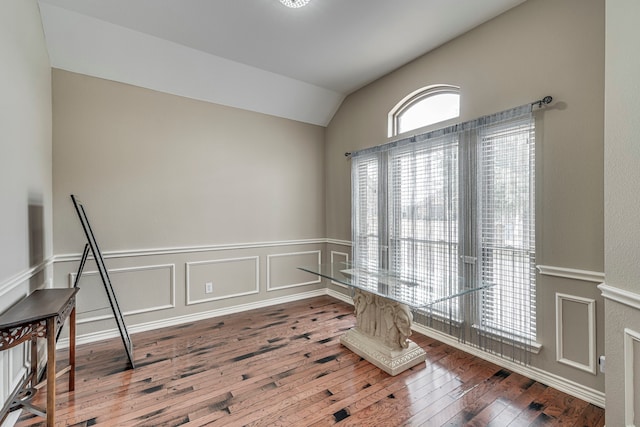 interior space with vaulted ceiling, a decorative wall, a wainscoted wall, and hardwood / wood-style floors