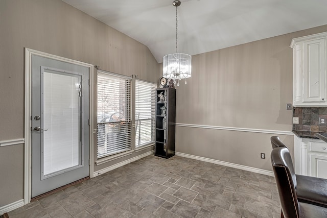 unfurnished dining area with lofted ceiling, a notable chandelier, baseboards, and stone finish flooring