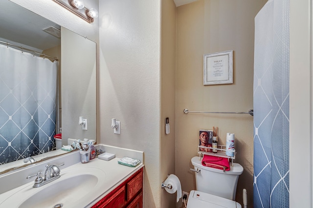 full bath with visible vents, toilet, vanity, and a textured wall