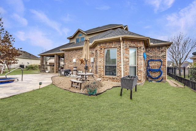 rear view of property with fence, brick siding, a lawn, and a patio area