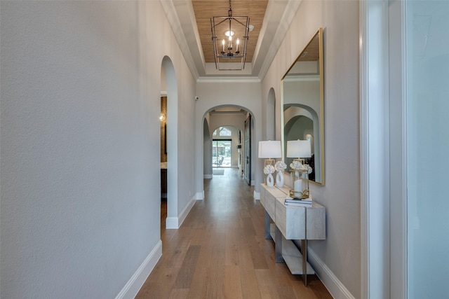 corridor featuring an inviting chandelier, a tray ceiling, light hardwood / wood-style flooring, and crown molding