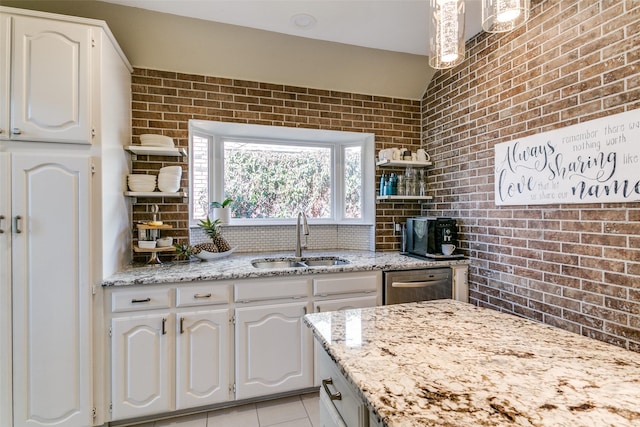 kitchen featuring stainless steel dishwasher, brick wall, white cabinetry, and a sink