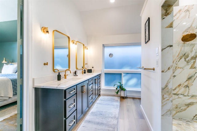 ensuite bathroom with double vanity, ensuite bathroom, vaulted ceiling, a sink, and wood finished floors