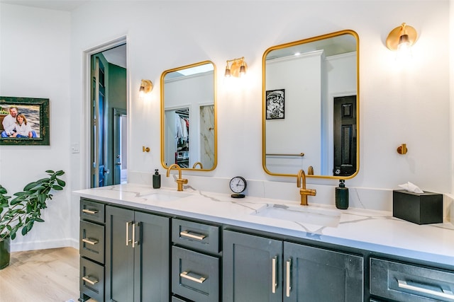 full bath featuring wood finished floors, a sink, baseboards, and double vanity