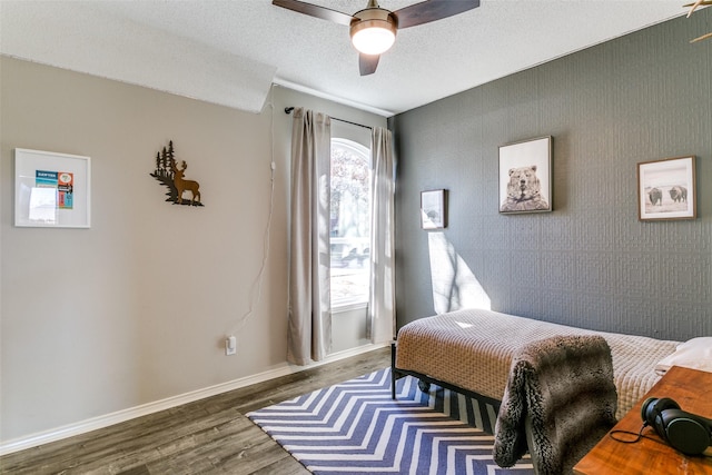 bedroom with baseboards, dark wood-style floors, ceiling fan, an accent wall, and a textured ceiling