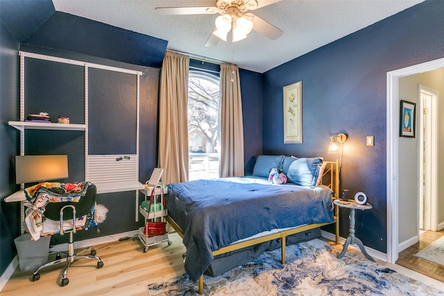 bedroom with a ceiling fan, a textured ceiling, baseboards, and wood finished floors