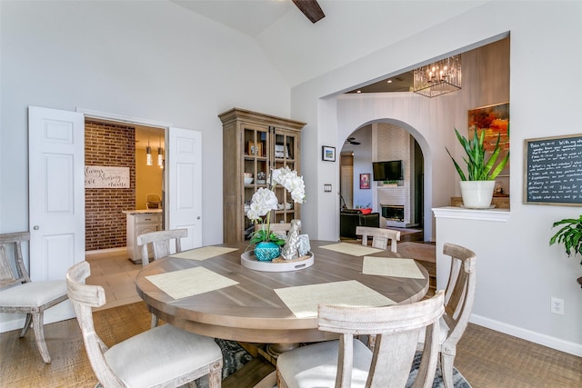 dining room with arched walkways, a notable chandelier, a fireplace, high vaulted ceiling, and baseboards