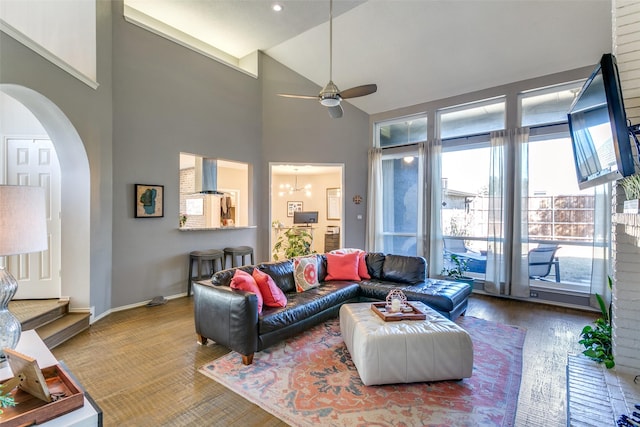 living area with arched walkways, high vaulted ceiling, ceiling fan with notable chandelier, wood finished floors, and baseboards