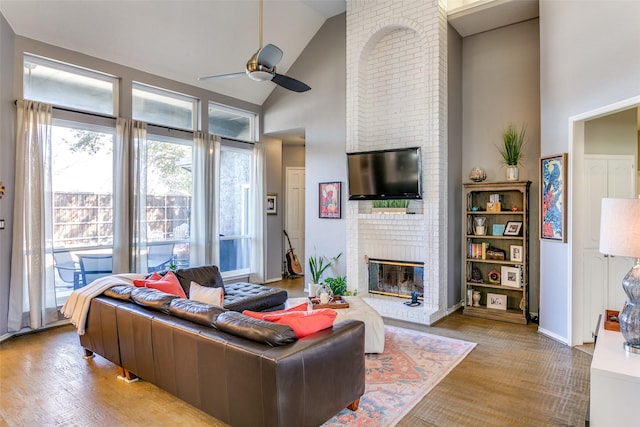 living room featuring a brick fireplace, ceiling fan, high vaulted ceiling, light wood-type flooring, and baseboards