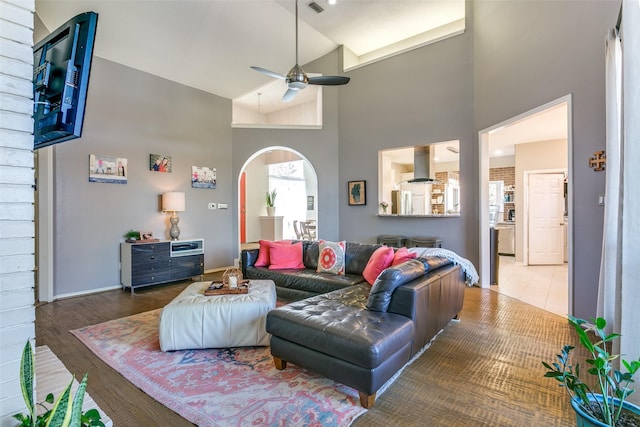 living area featuring arched walkways, a ceiling fan, wood finished floors, high vaulted ceiling, and baseboards