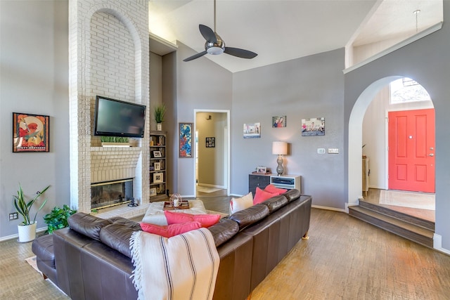 living area featuring high vaulted ceiling, a brick fireplace, ceiling fan, and baseboards