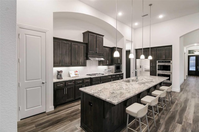 kitchen featuring sink, a breakfast bar area, built in appliances, hanging light fixtures, and an island with sink