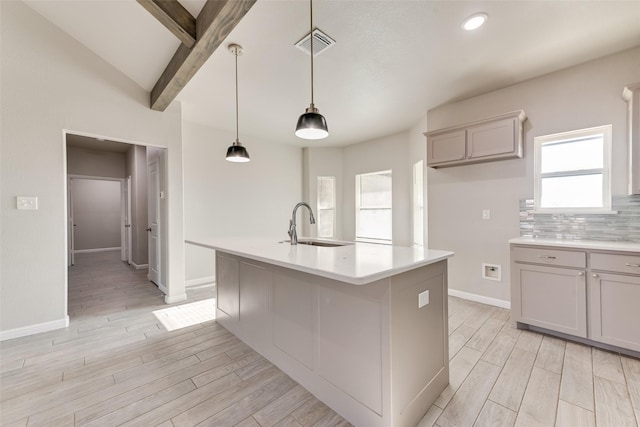 kitchen featuring decorative light fixtures, beamed ceiling, sink, backsplash, and a kitchen island with sink