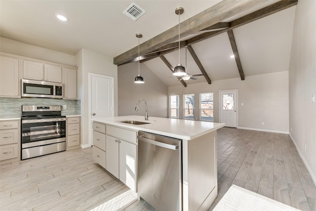 kitchen featuring an island with sink, sink, vaulted ceiling with beams, hanging light fixtures, and stainless steel appliances