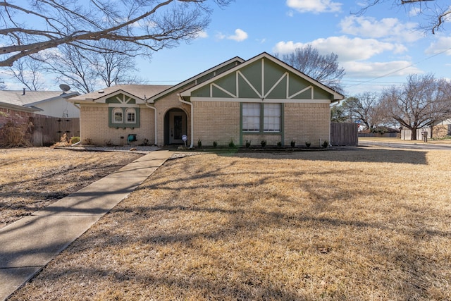 tudor home featuring fence, a front lawn, and brick siding