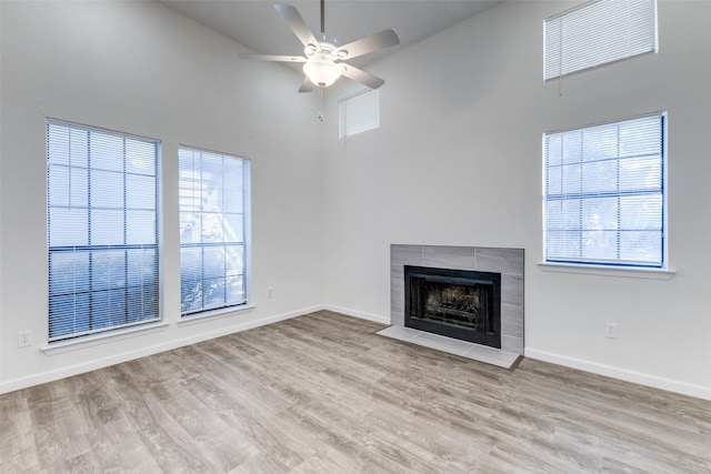 unfurnished living room featuring a tiled fireplace, ceiling fan, a high ceiling, and light wood-type flooring