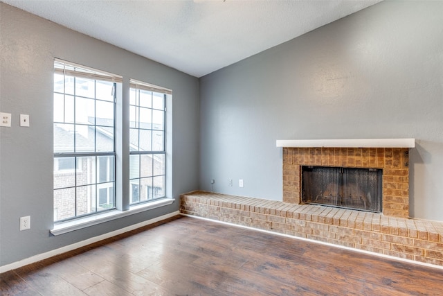 unfurnished living room with a wealth of natural light, a brick fireplace, baseboards, and dark wood-style flooring