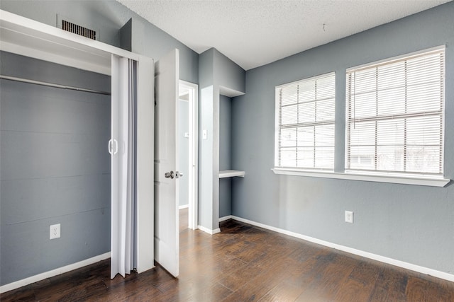 unfurnished bedroom with dark wood-type flooring, visible vents, a textured ceiling, and baseboards