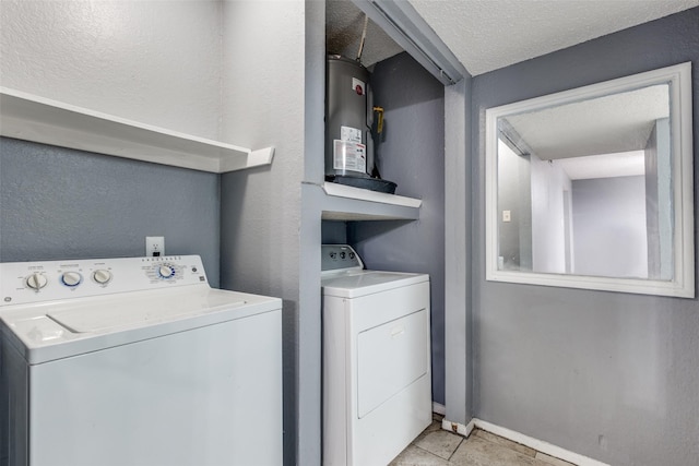 washroom featuring laundry area, baseboards, washing machine and clothes dryer, a textured ceiling, and water heater