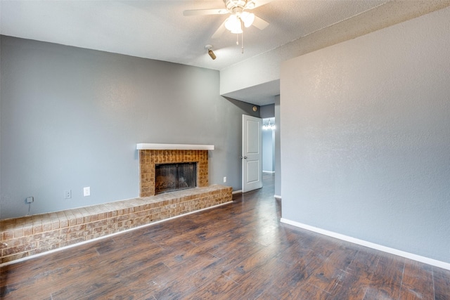 unfurnished living room featuring dark wood-style flooring, a brick fireplace, a ceiling fan, and baseboards