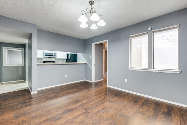 empty room with a notable chandelier, a textured ceiling, baseboards, and dark wood-style flooring