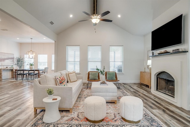 living room with ceiling fan with notable chandelier, light hardwood / wood-style flooring, high vaulted ceiling, and beamed ceiling