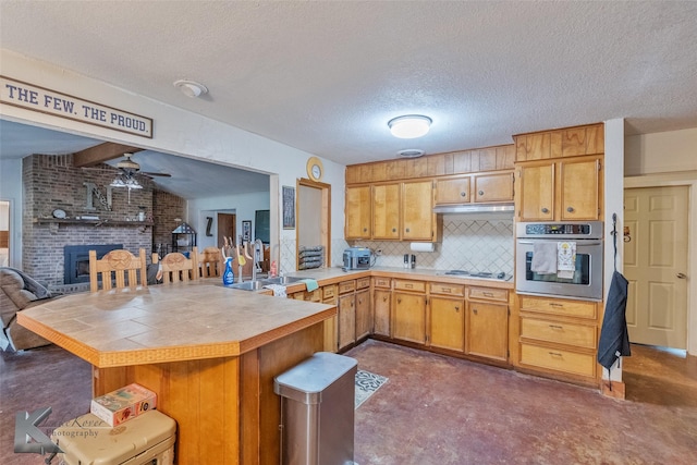 kitchen with sink, a brick fireplace, kitchen peninsula, oven, and decorative backsplash