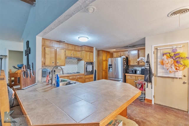 kitchen with appliances with stainless steel finishes, tile counters, sink, and decorative backsplash