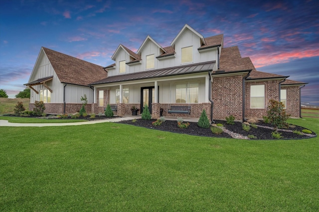 view of front of home with a lawn, covered porch, a standing seam roof, board and batten siding, and brick siding