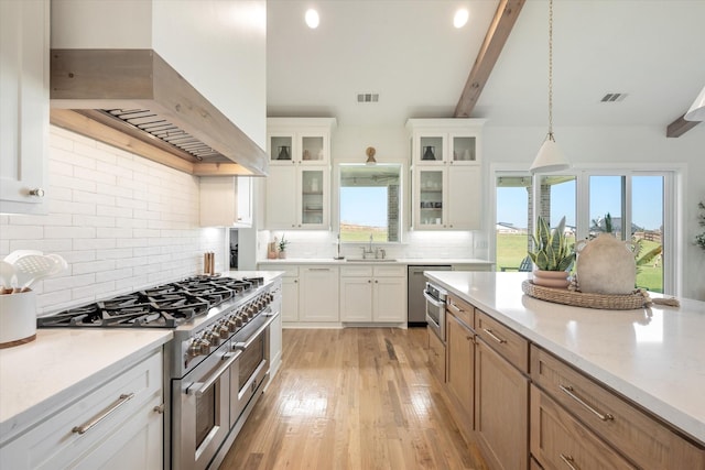 kitchen featuring range with two ovens, custom range hood, glass insert cabinets, hanging light fixtures, and white cabinetry