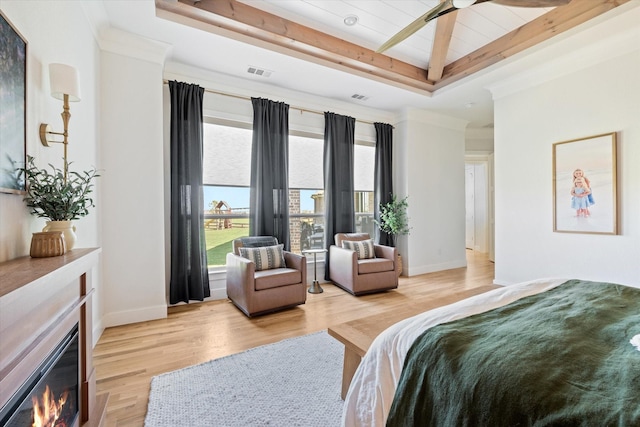 bedroom with a glass covered fireplace, light wood-type flooring, a raised ceiling, and visible vents