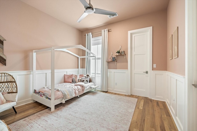 bedroom with a wainscoted wall, ceiling fan, and wood finished floors