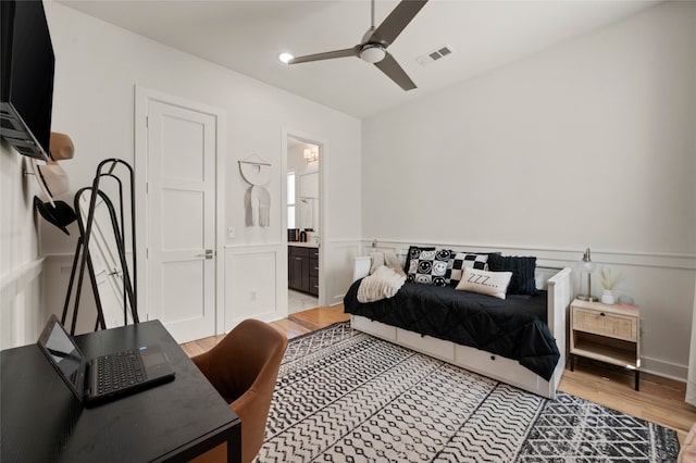 bedroom featuring ensuite bathroom, wainscoting, light wood-type flooring, and visible vents