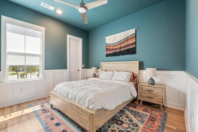 bedroom featuring a ceiling fan, light wood-type flooring, a wainscoted wall, and visible vents