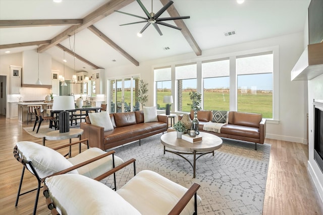 living area with light wood-style floors, a glass covered fireplace, visible vents, and beamed ceiling