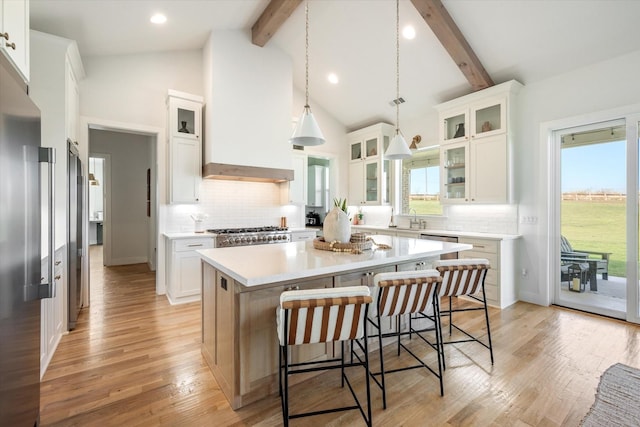 kitchen featuring a kitchen island, glass insert cabinets, light countertops, white cabinetry, and a sink