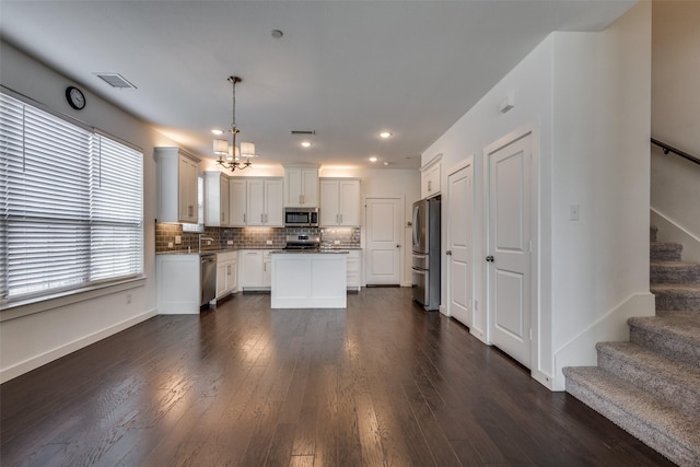 kitchen with a kitchen island, pendant lighting, white cabinets, stainless steel appliances, and dark wood-type flooring