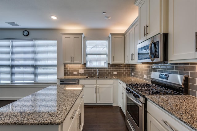 kitchen with sink, white cabinetry, light stone counters, appliances with stainless steel finishes, and dark hardwood / wood-style floors