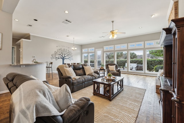 living room featuring ceiling fan with notable chandelier, light wood-type flooring, and ornamental molding