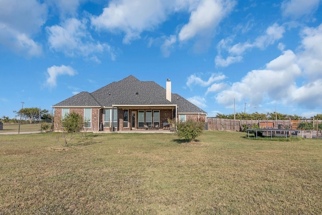 back of property with a trampoline, a patio, and a lawn