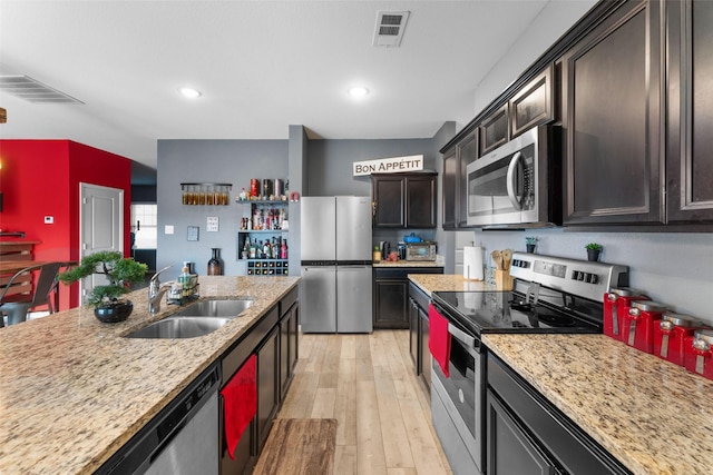 kitchen with appliances with stainless steel finishes, sink, dark brown cabinetry, light stone counters, and light hardwood / wood-style floors