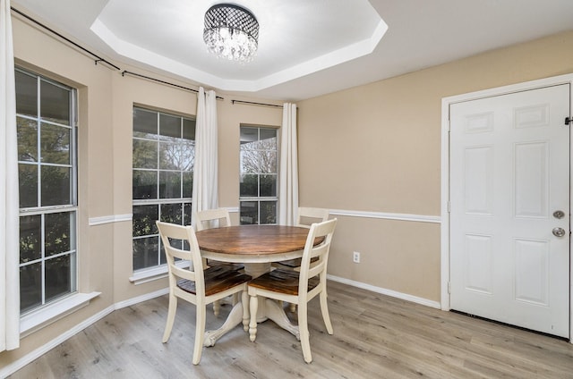 dining room with light hardwood / wood-style flooring, an inviting chandelier, and a tray ceiling