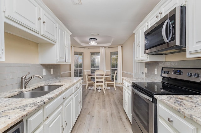 kitchen with sink, white cabinets, light stone counters, stainless steel appliances, and light hardwood / wood-style flooring