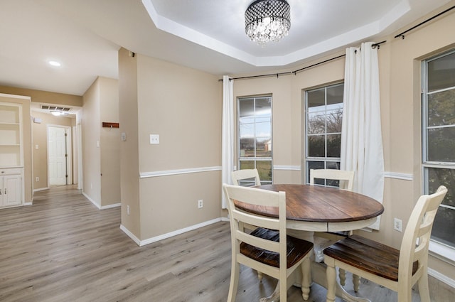 dining space with a raised ceiling, a notable chandelier, and light hardwood / wood-style floors