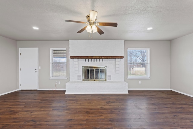 unfurnished living room with ceiling fan, a brick fireplace, dark wood-type flooring, and a textured ceiling